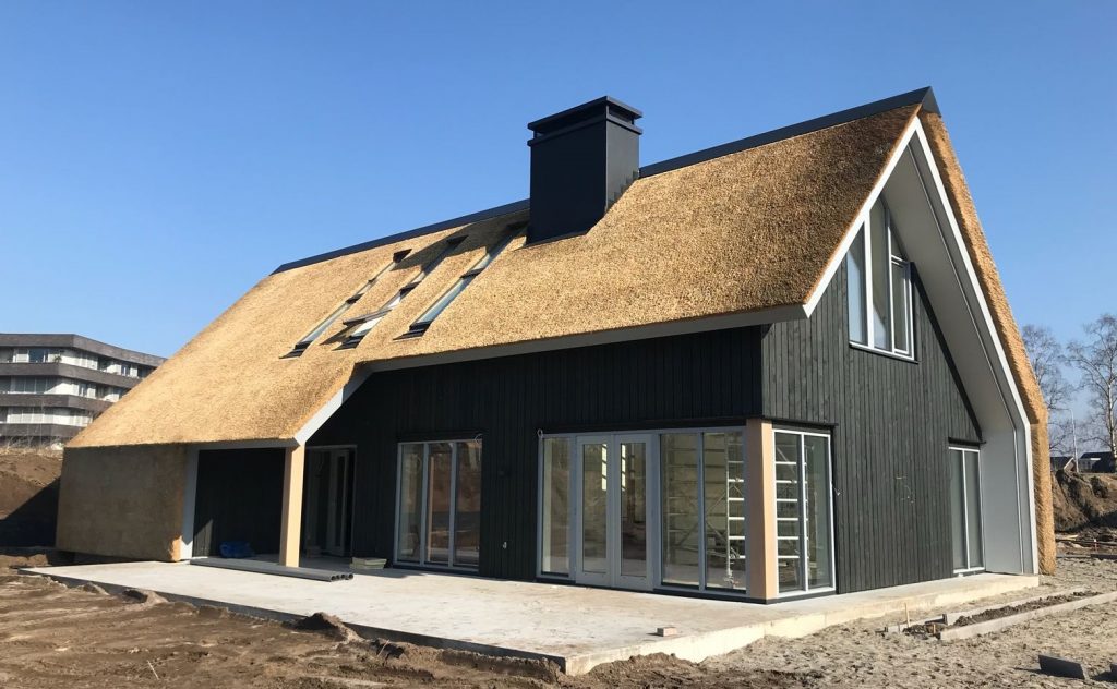 Tuinzijde moderne schuurwoning met riet en grote glasvlakken