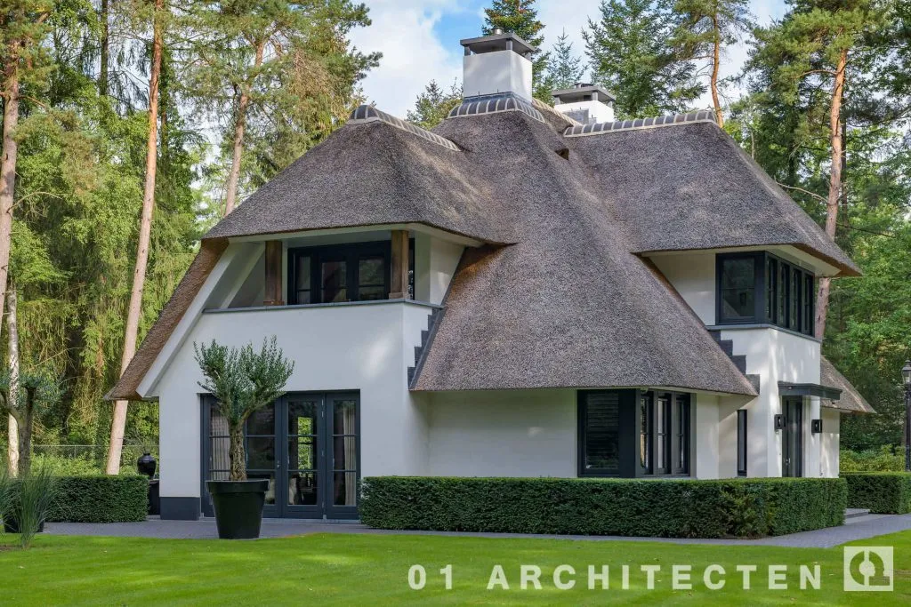 Rietgedekte villa in Ugchelen met asymmetrische kap, witte gevels en donkere kozijnen tussen de bomen