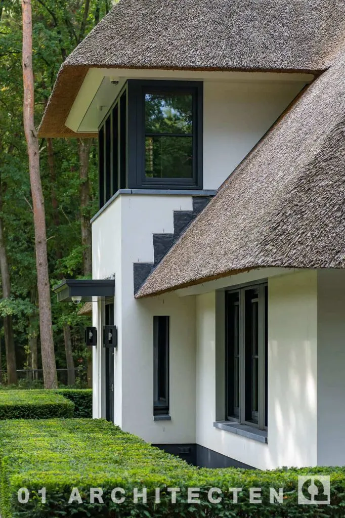 Detail van de villa met witte gevels, donkere kozijnen en de aansluiting op de rieten kap